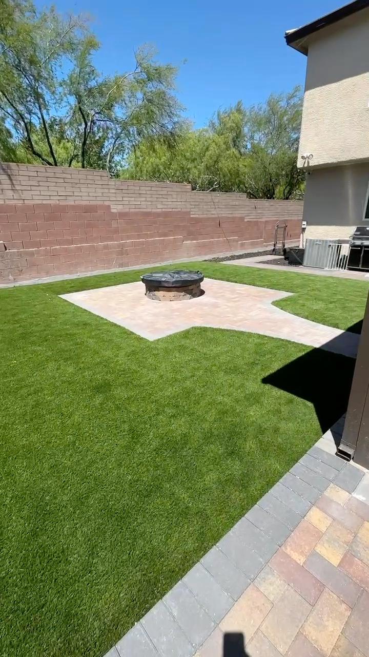 Synthetic turf lawn bordered by pavers around a backyard fire pit
